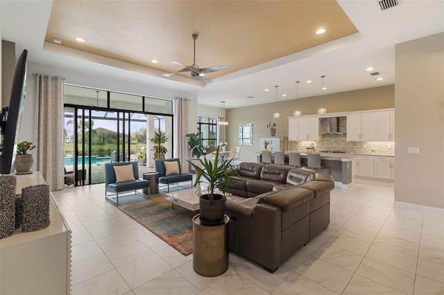 tiled living room featuring ceiling fan and a raised ceiling