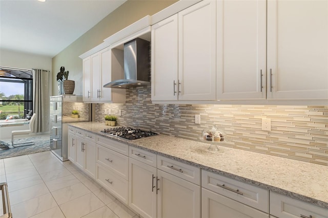 kitchen with stainless steel gas cooktop, tasteful backsplash, wall chimney range hood, light stone countertops, and white cabinets