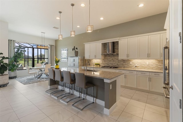 kitchen with sink, gas cooktop, a kitchen island with sink, stone countertops, and wall chimney exhaust hood