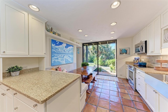 kitchen with appliances with stainless steel finishes, white cabinetry, light stone counters, and tasteful backsplash