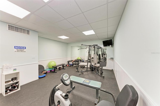 exercise room with a paneled ceiling, wainscoting, and visible vents