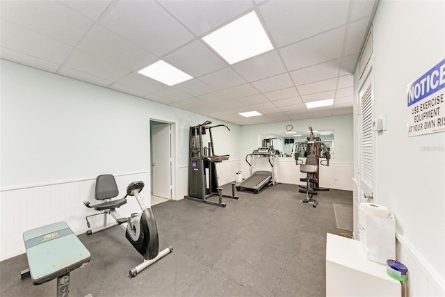 gym featuring a paneled ceiling and a wainscoted wall