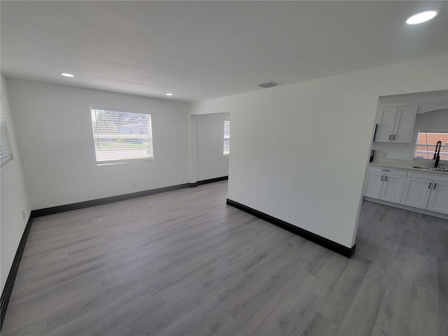 empty room with sink, light wood-type flooring, and a healthy amount of sunlight