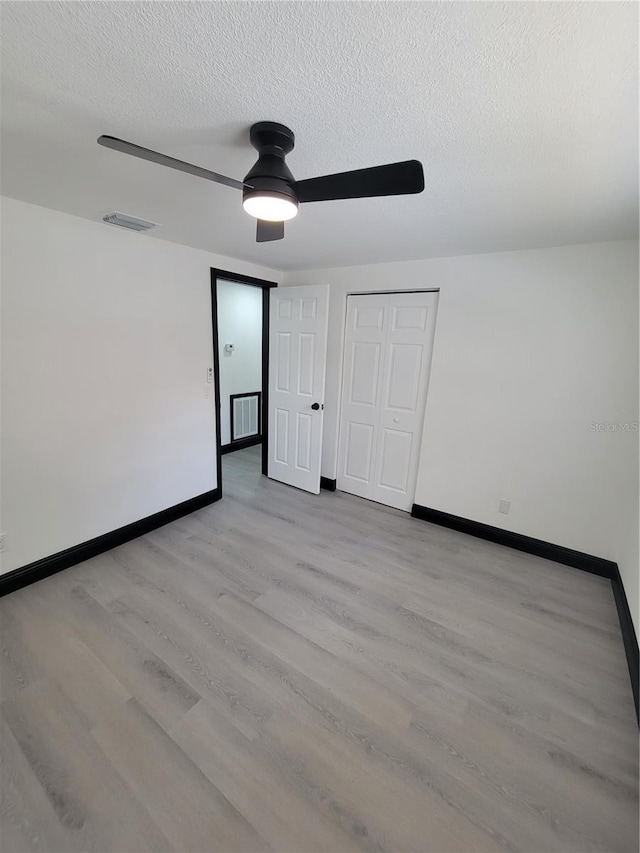 unfurnished bedroom featuring ceiling fan, a textured ceiling, a closet, and light wood-type flooring