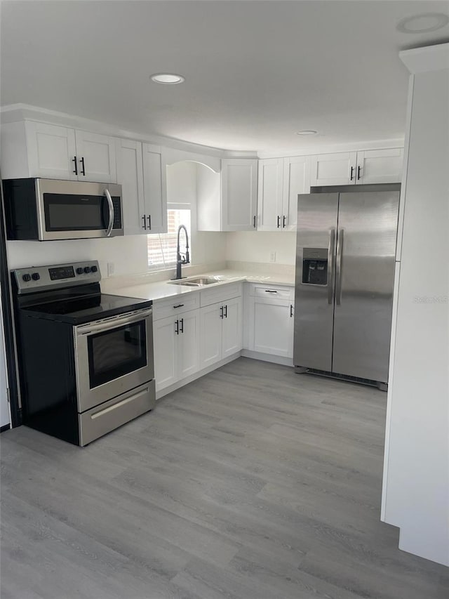 kitchen with sink, stainless steel appliances, white cabinets, and light wood-type flooring