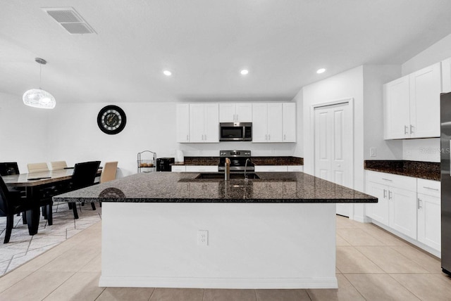 kitchen with appliances with stainless steel finishes, dark stone counters, sink, decorative light fixtures, and an island with sink