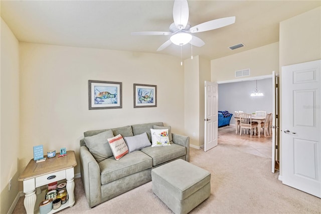 living room featuring ceiling fan with notable chandelier, baseboards, visible vents, and light colored carpet