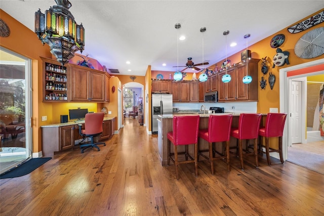 kitchen with built in desk, hanging light fixtures, a center island with sink, appliances with stainless steel finishes, and dark hardwood / wood-style flooring