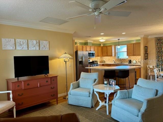 living room with ceiling fan, sink, a textured ceiling, and ornamental molding