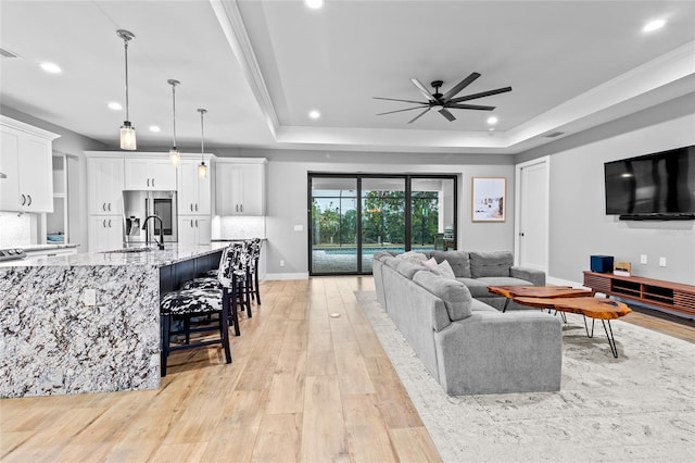 living room with ceiling fan, light hardwood / wood-style floors, sink, crown molding, and a tray ceiling