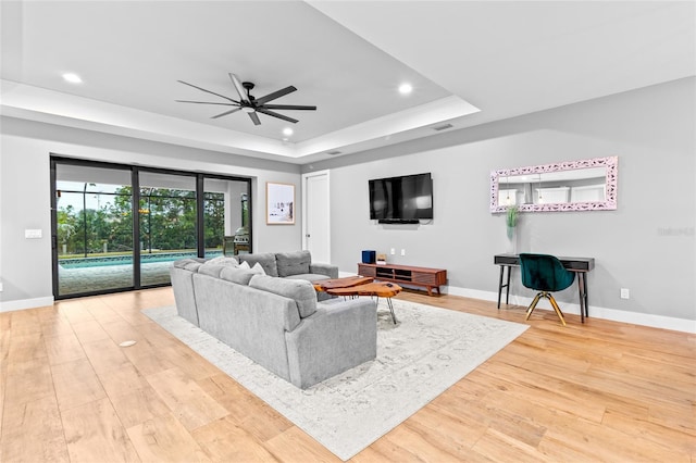 living room featuring light wood-type flooring, ceiling fan, and a tray ceiling