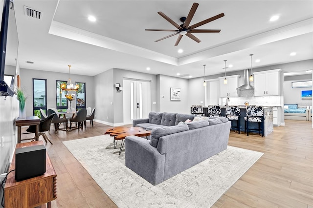 living room with ceiling fan with notable chandelier, sink, light hardwood / wood-style flooring, and a raised ceiling