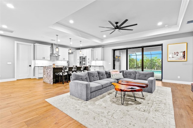 living room with ceiling fan, light hardwood / wood-style flooring, and a raised ceiling