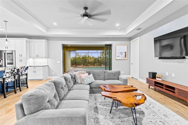 living room featuring a raised ceiling, ceiling fan, ornamental molding, and light hardwood / wood-style floors