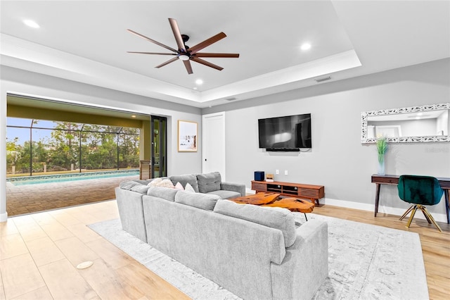 living room with ceiling fan, a tray ceiling, and light hardwood / wood-style floors