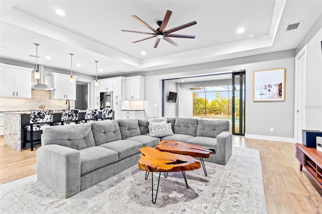 living room featuring ceiling fan, a tray ceiling, light hardwood / wood-style flooring, and crown molding