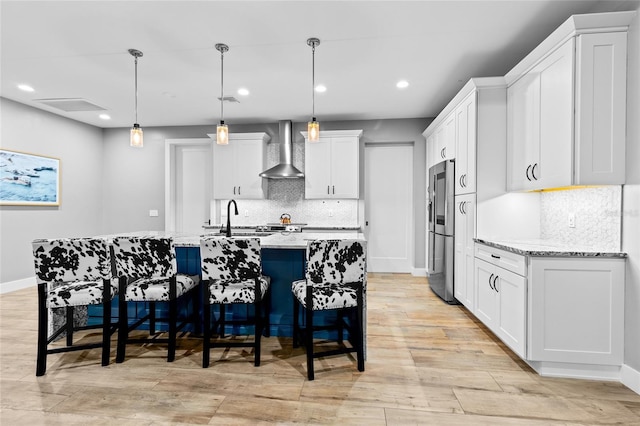 kitchen featuring decorative light fixtures, decorative backsplash, white cabinets, wall chimney exhaust hood, and light stone counters