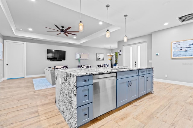 kitchen featuring decorative light fixtures, dishwasher, a raised ceiling, an island with sink, and light stone counters