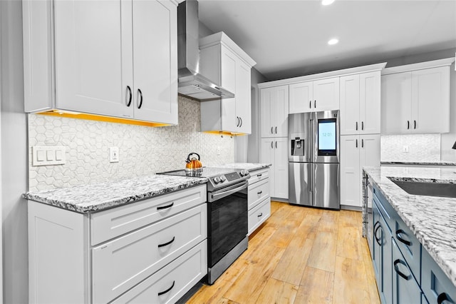 kitchen with sink, white cabinetry, light stone countertops, stainless steel appliances, and wall chimney exhaust hood