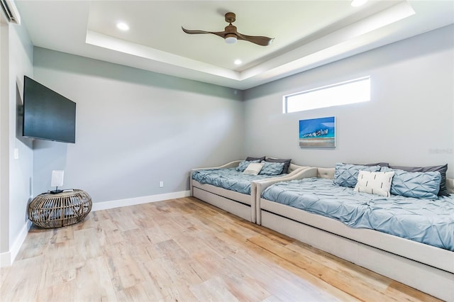 bedroom with ceiling fan, wood-type flooring, and a tray ceiling