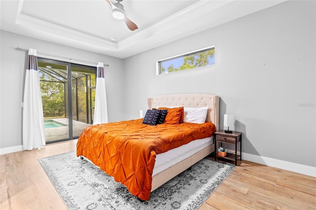 bedroom with ceiling fan, access to outside, a tray ceiling, hardwood / wood-style flooring, and ornamental molding