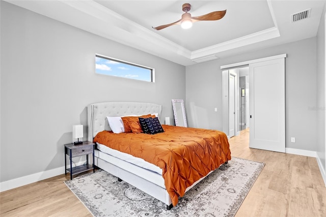 bedroom featuring ceiling fan, crown molding, light hardwood / wood-style flooring, and a tray ceiling