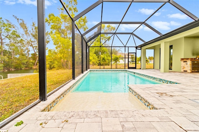 view of pool with a patio area, a lawn, glass enclosure, a water view, and an outdoor kitchen