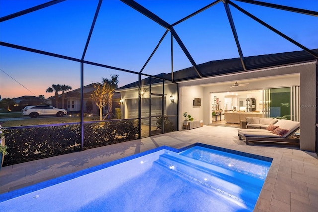 pool at dusk featuring glass enclosure, a patio area, an outdoor hangout area, and ceiling fan