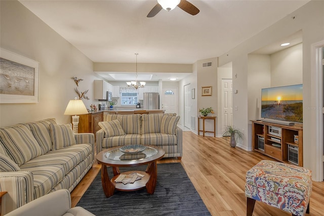 living room featuring ceiling fan with notable chandelier and light wood-type flooring