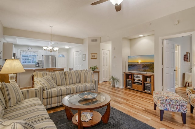 living room featuring ceiling fan with notable chandelier and light hardwood / wood-style flooring