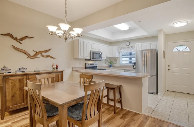 dining area featuring light hardwood / wood-style flooring, a notable chandelier, and a raised ceiling