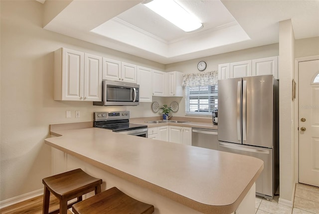 kitchen with a kitchen breakfast bar, white cabinets, kitchen peninsula, stainless steel appliances, and a tray ceiling