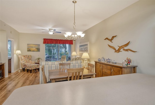 dining room featuring ceiling fan with notable chandelier and light hardwood / wood-style flooring