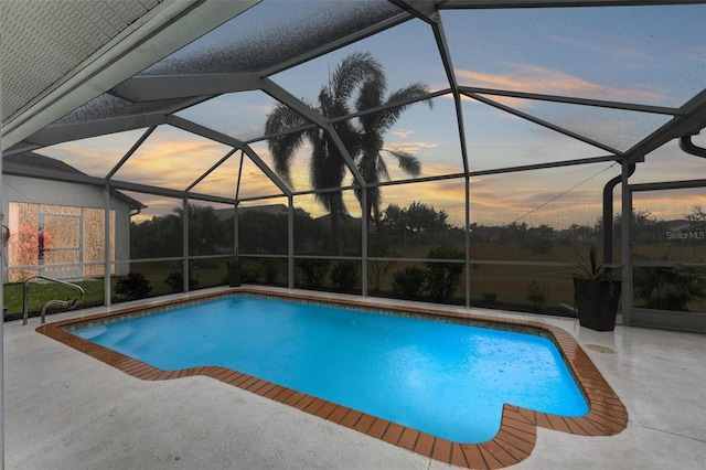 pool at dusk featuring glass enclosure and a patio area