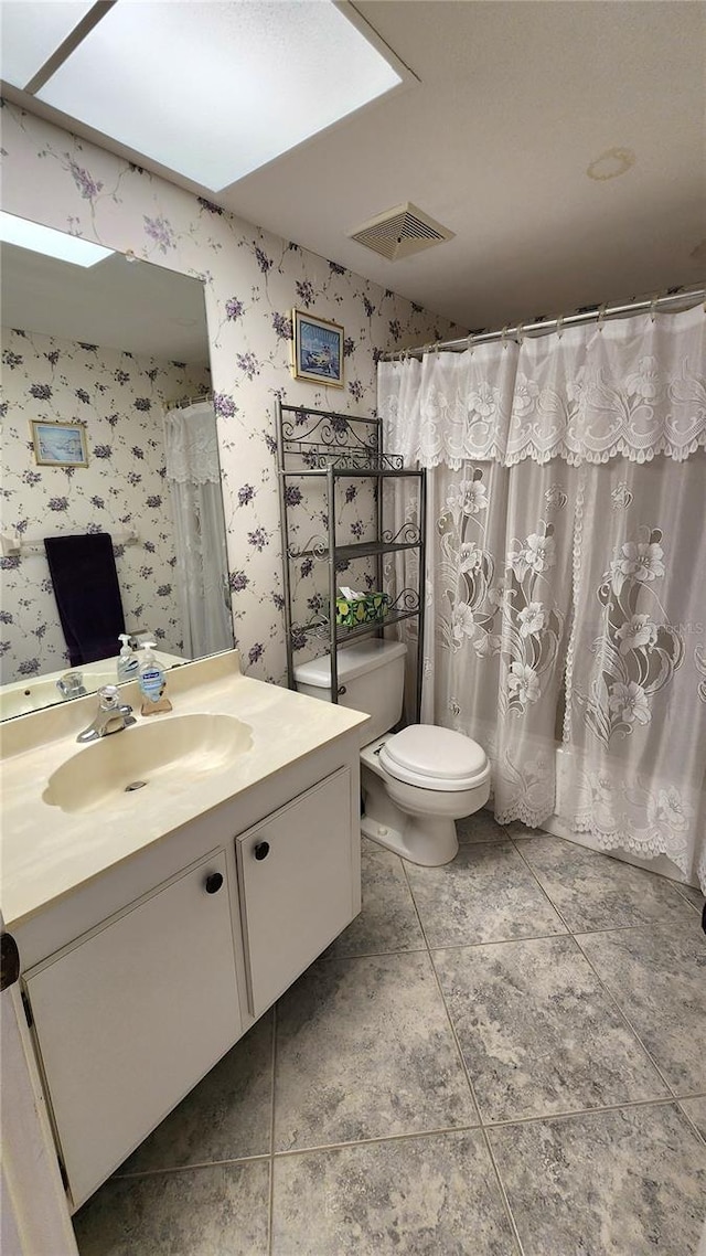 bathroom with toilet, vanity, tile patterned floors, and a skylight