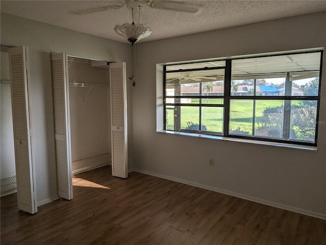 unfurnished bedroom with ceiling fan, dark hardwood / wood-style floors, a textured ceiling, and two closets