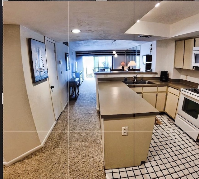 kitchen featuring cream cabinets, a peninsula, white appliances, a sink, and dark countertops