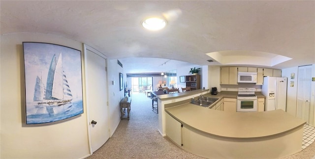 kitchen with cream cabinets, light carpet, a peninsula, white appliances, and a sink