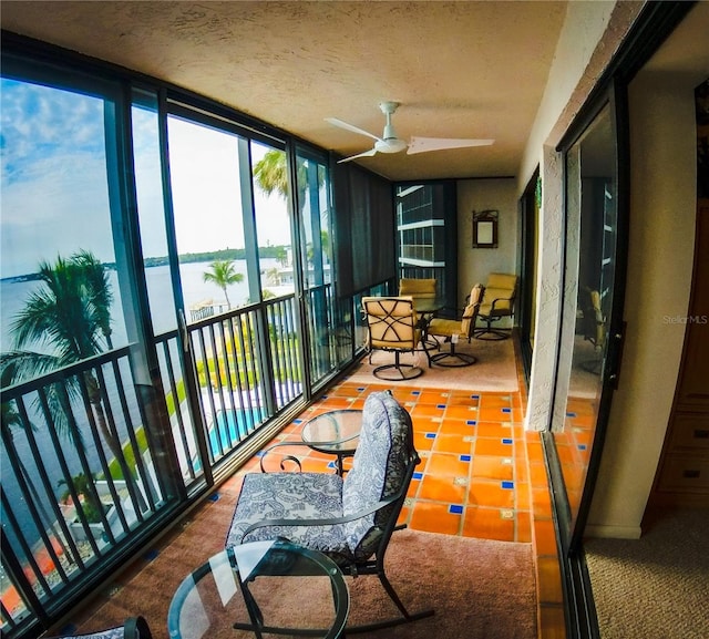 sunroom with a ceiling fan and a water view