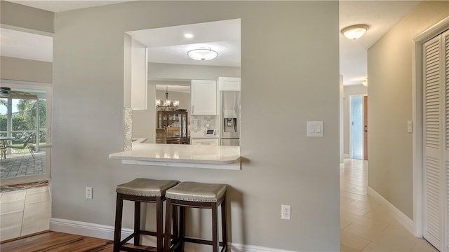 kitchen with a breakfast bar area, white cabinetry, stainless steel fridge, kitchen peninsula, and backsplash