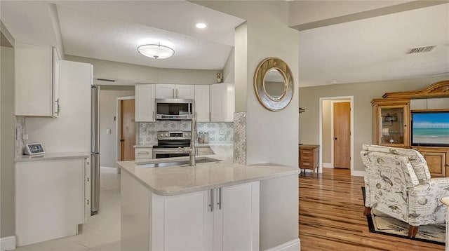 kitchen with sink, white cabinetry, kitchen peninsula, stainless steel appliances, and backsplash