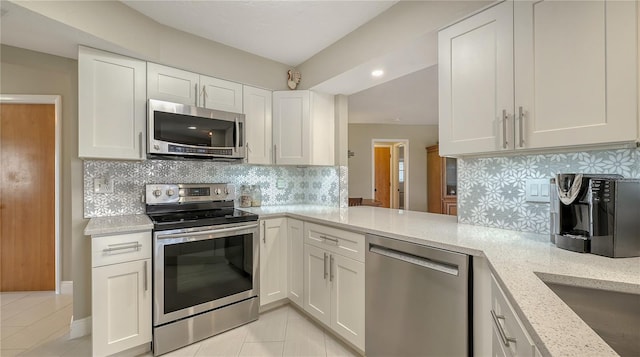 kitchen featuring appliances with stainless steel finishes, white cabinetry, light stone counters, light tile patterned flooring, and kitchen peninsula