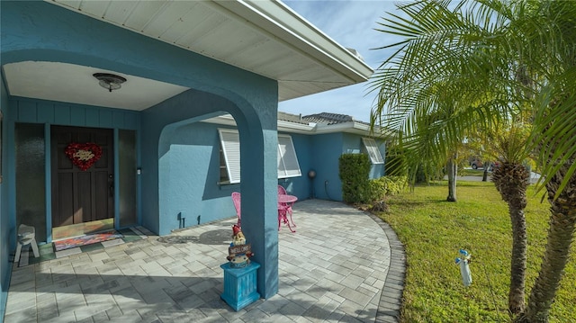 entrance to property featuring a lawn and a patio