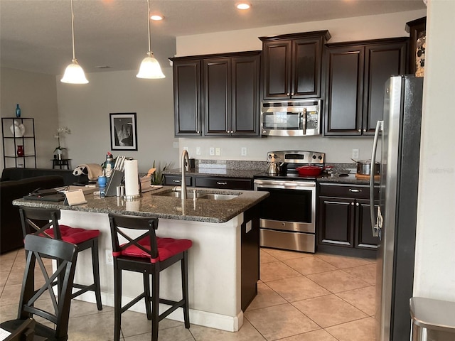 kitchen with a breakfast bar, sink, dark stone countertops, hanging light fixtures, and stainless steel appliances