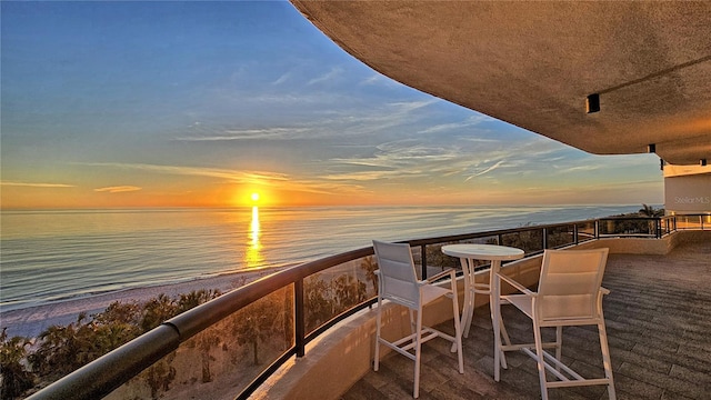 balcony at dusk featuring a water view and a view of the beach