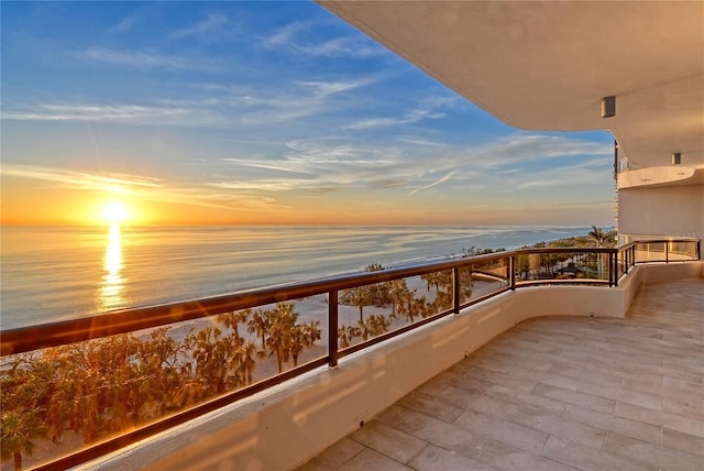 balcony at dusk featuring a water view