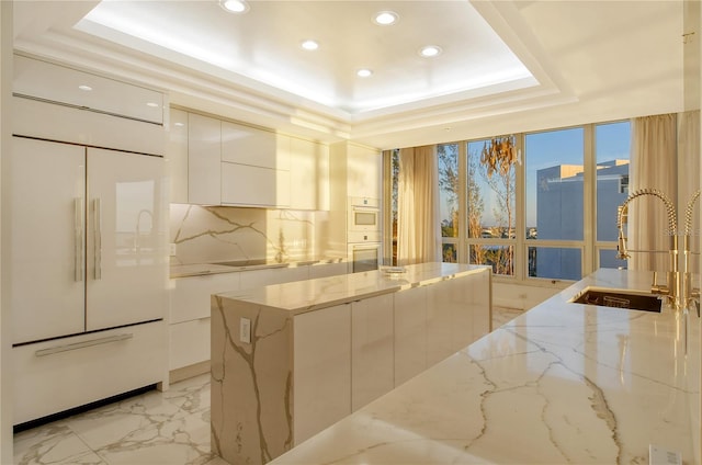 kitchen with white cabinetry, sink, a tray ceiling, light stone countertops, and paneled refrigerator