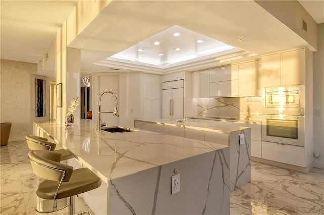 kitchen featuring sink, white cabinets, a kitchen breakfast bar, light stone counters, and paneled fridge