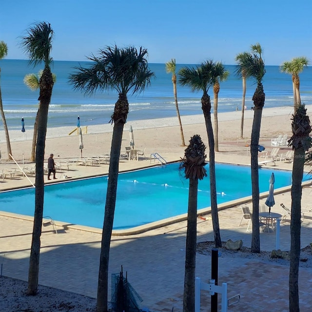 view of swimming pool with a patio area, a water view, and a view of the beach