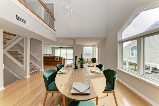 dining area with a notable chandelier, a towering ceiling, and light hardwood / wood-style floors